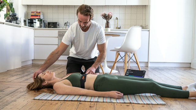 Person demonstrating a supported pelvic release exercise using a yoga block under the sacrum