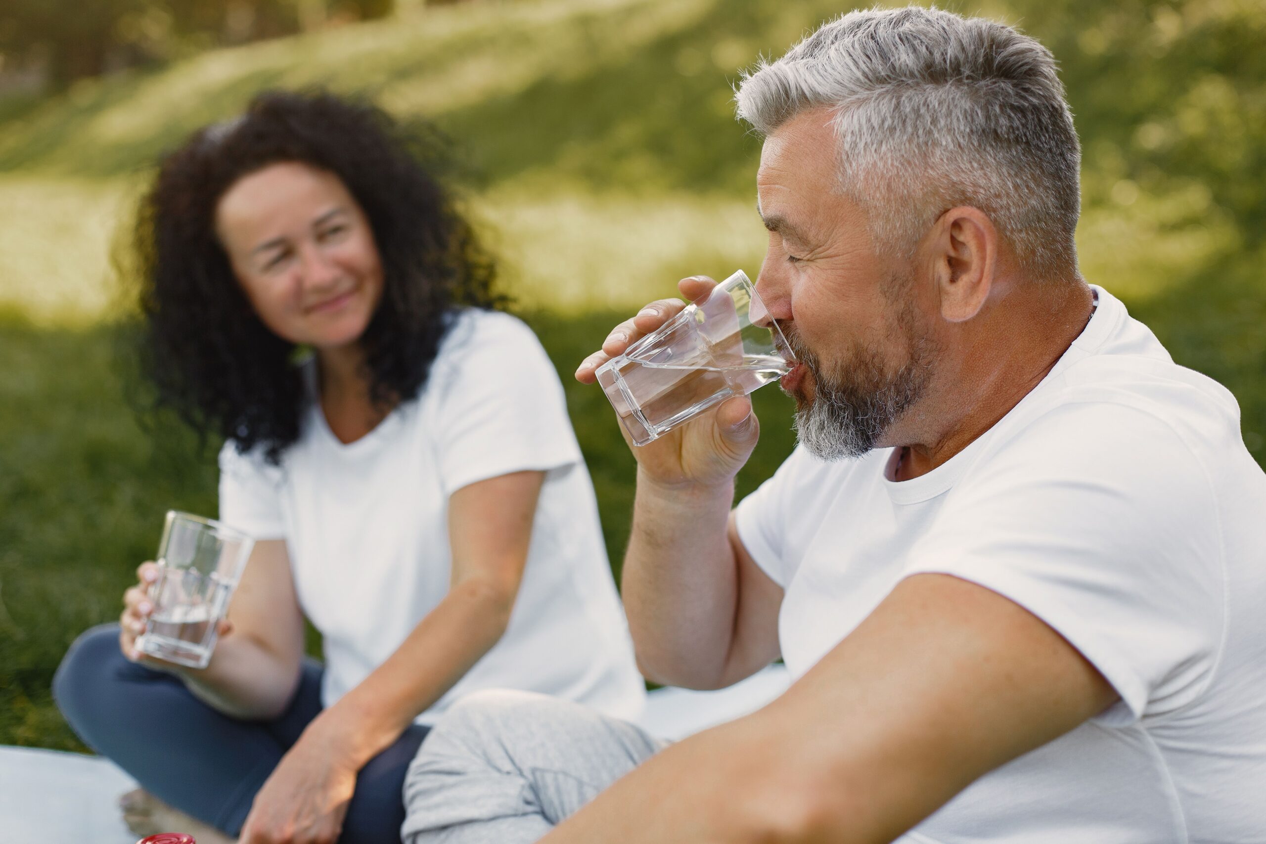 Older adult drinking water on a warm day while experiencing symptoms of possible dehydration
