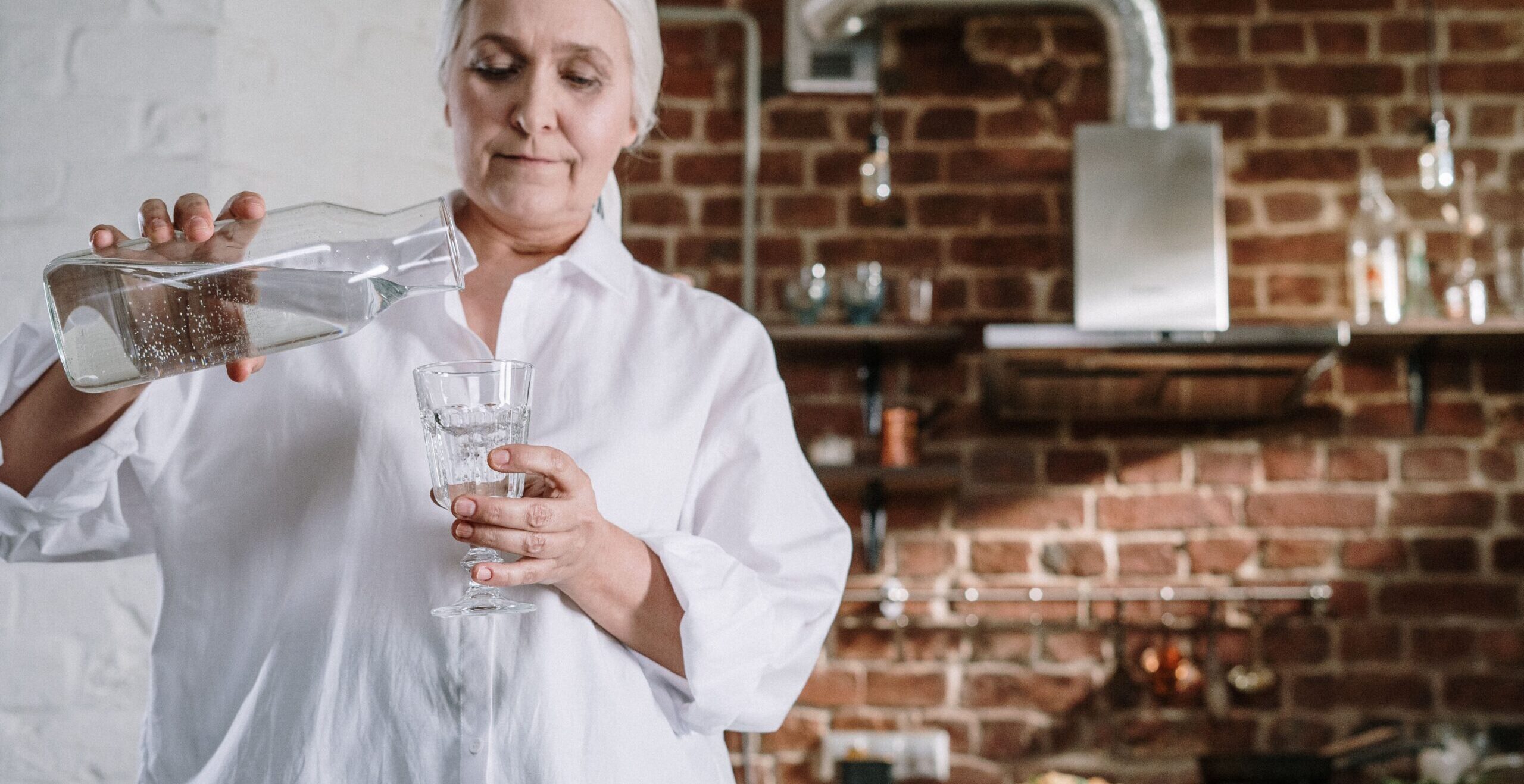 Older adult drinking a glass of water at home while staying hydrated