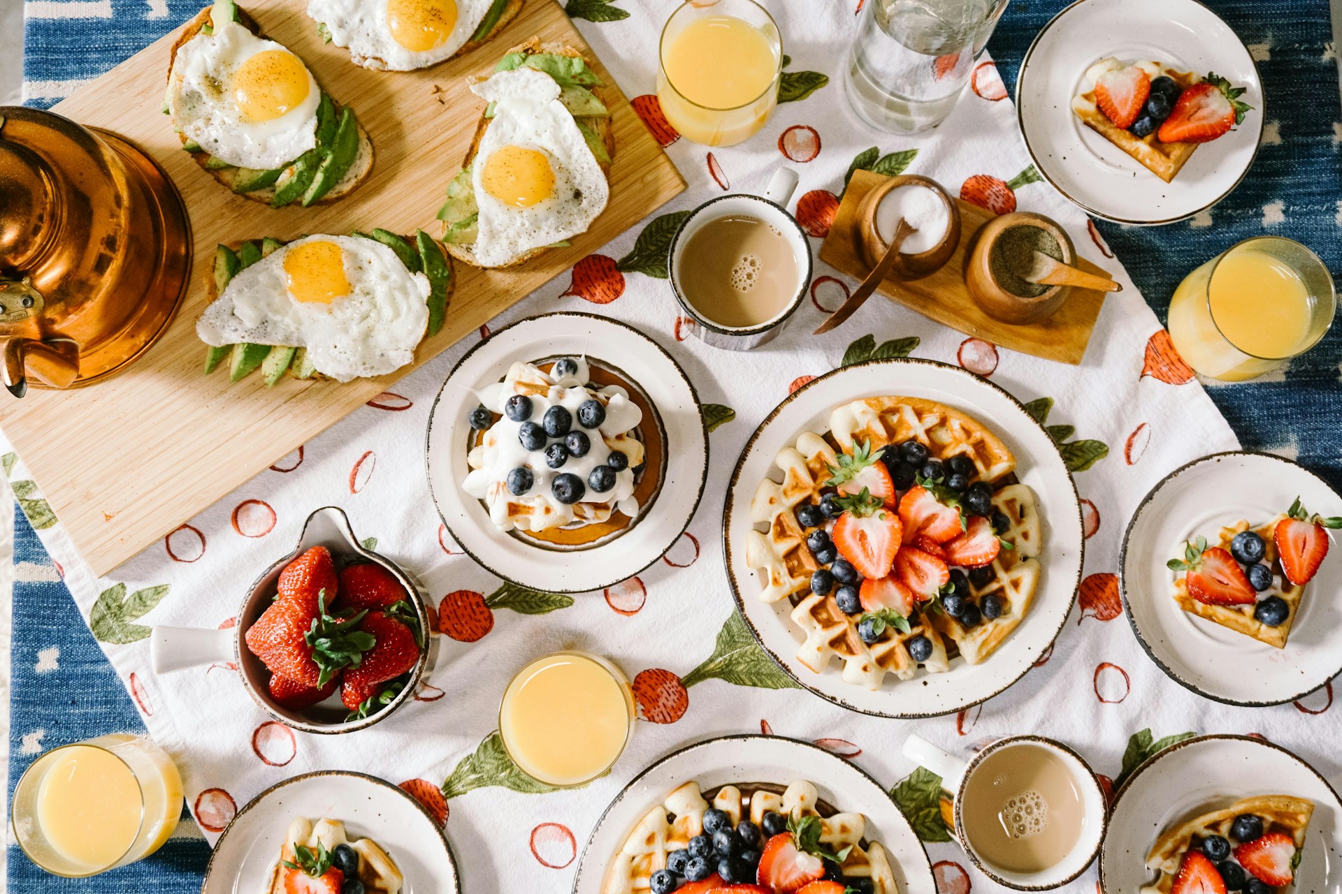 A bowl of oatmeal topped with fresh fruit and seeds beside a warm drink on a kitchen table